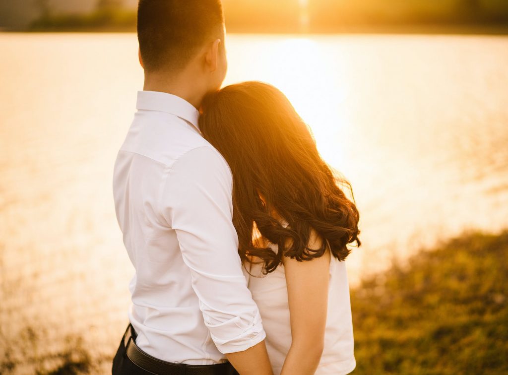 woman hugging man in front of body of water