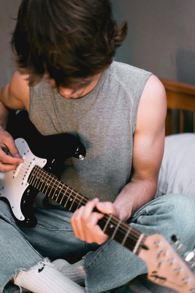 man in gray tank top playing white stratocaster electric guitar