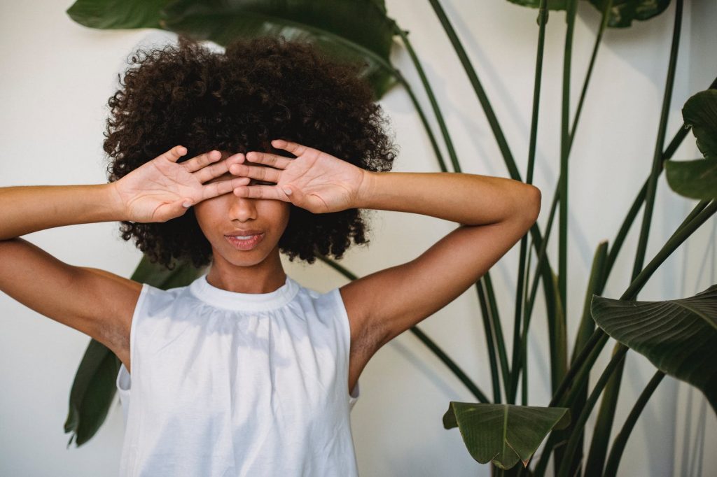 black woman covering face with hands standing near potted plant