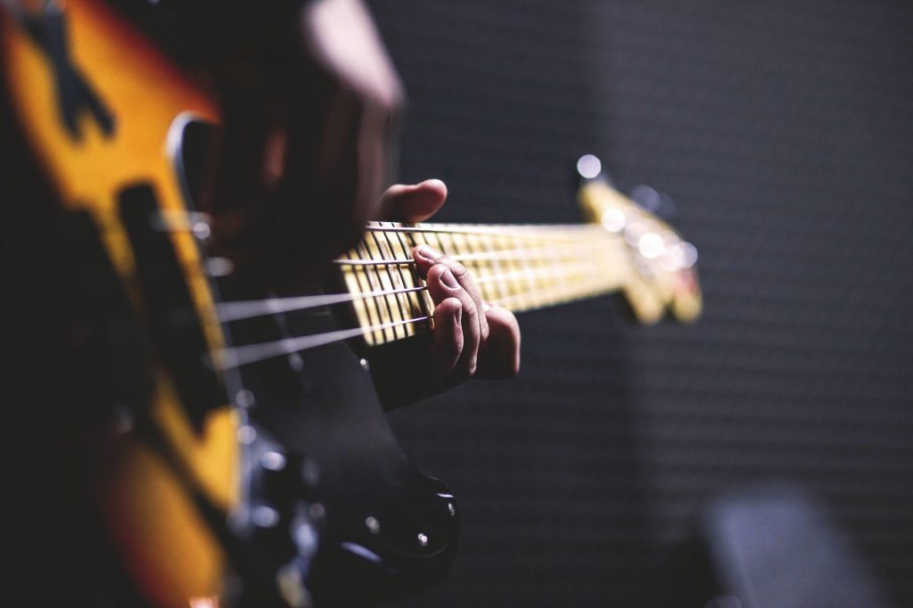 person playing sun burst electric bass guitar in bokeh photography